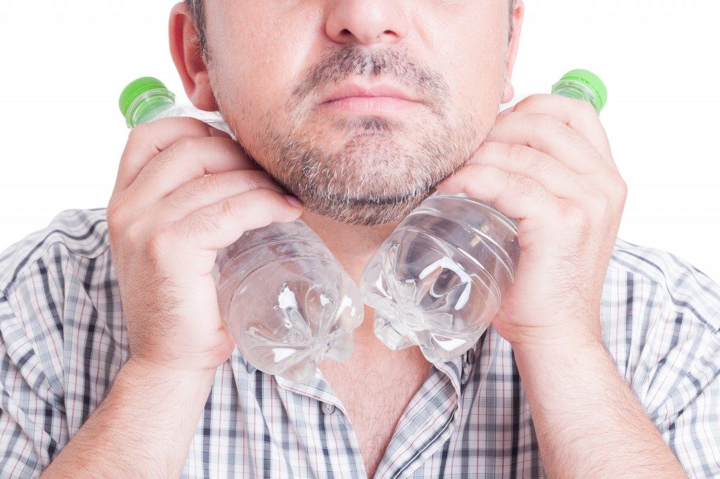 Man cooling his neck using cold water plastic bottles.