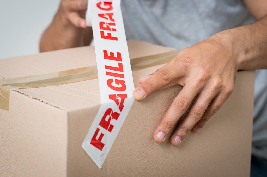 person putting fragile tape over boxed belonging