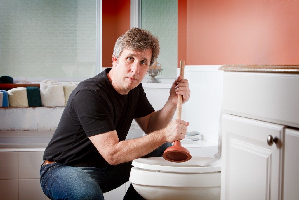 Man using a plunger to clear a plugged toilet