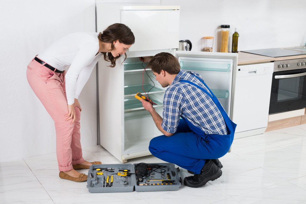 Beautiful Housewife Looking At Male Worker Repairing Refrigerator