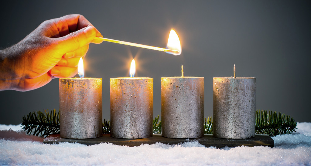 A hand holding a match to light four candles