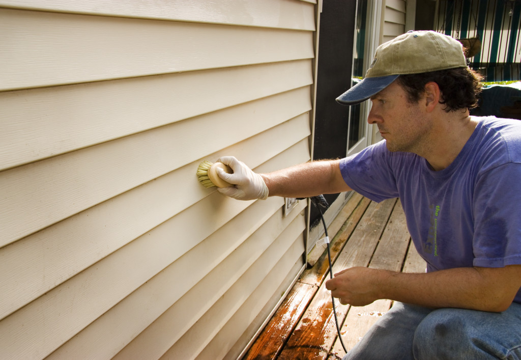 A man cleaning home siding with a brush