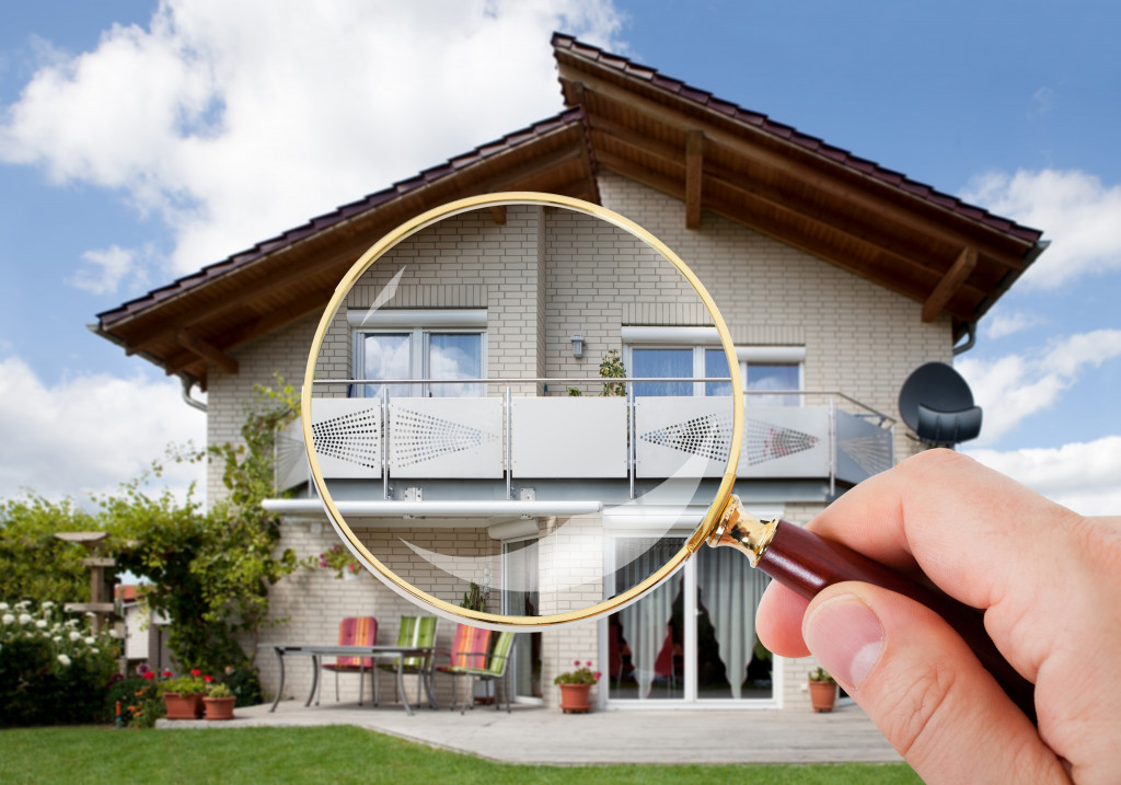 A hand holding a magnifying glass over a house