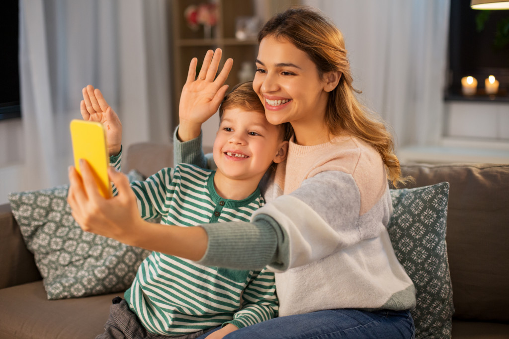 Mother and son waving hands while having a video call on a smartphone.