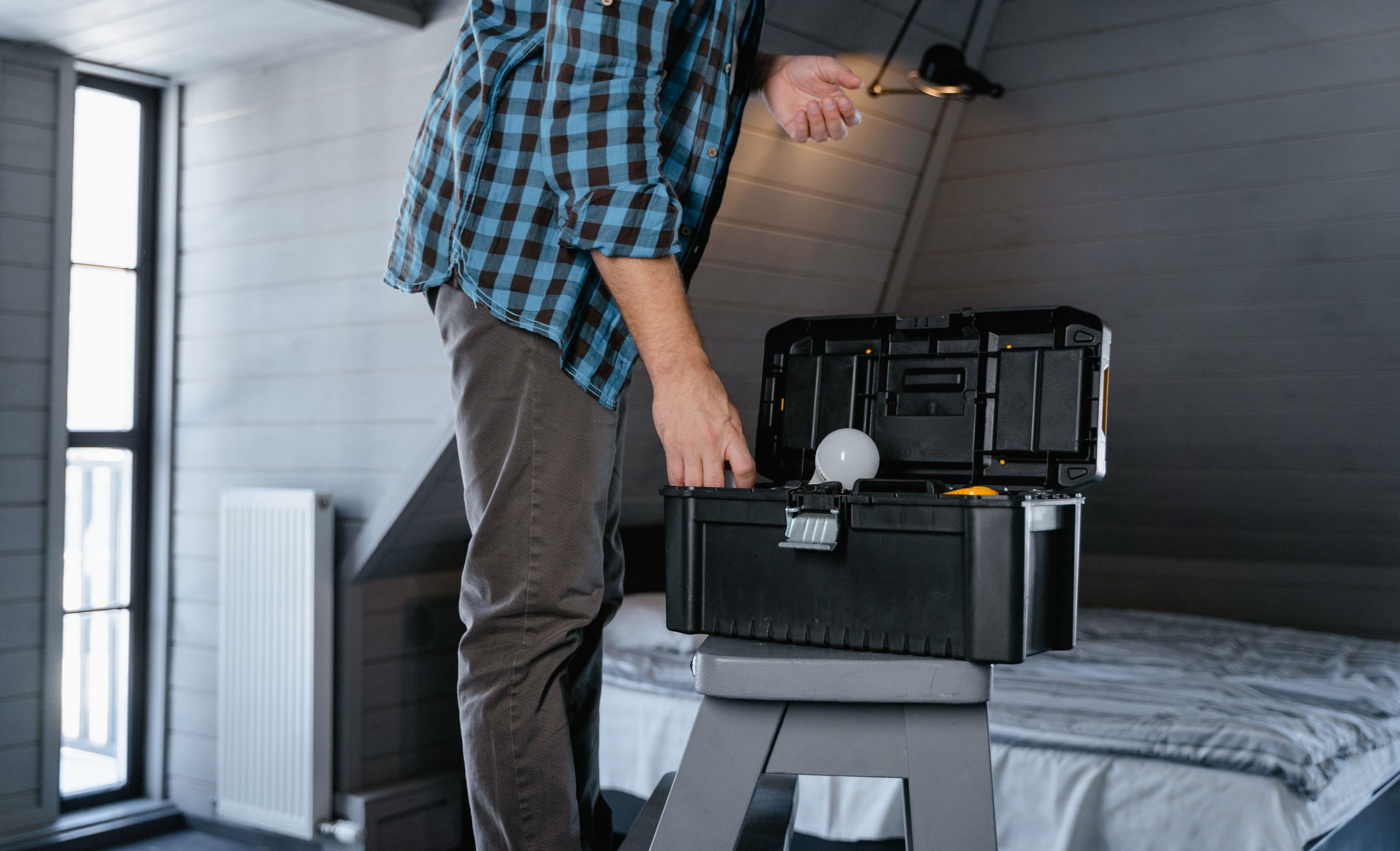 man inspecting an attic, standing on a ladder with a toolbox